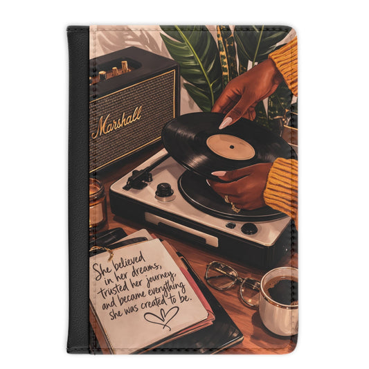 A vertical travel-style clutch or wallet with a black border, featuring a printed retro scene of a person placing a vinyl record on a turntable beside a Marshall amplifier, notebook, coffee cup, and plant leaves.