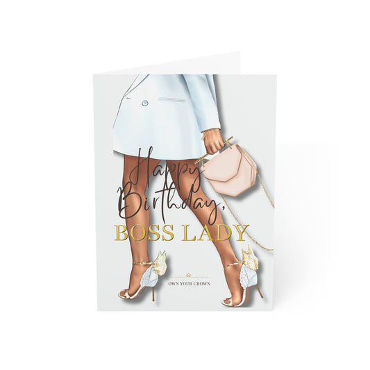 A folded greeting card standing upright on a white background. The card features an illustration of a woman's legs wearing a light blue blazer, beige tights, and high heels, holding a blush pink handbag.