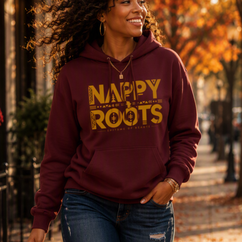 A woman walking barefoot on an autumn sidewalk wearing a maroon hoodie with 'NAPPY ROOTS' printed in yellow across the chest, paired with distressed blue jeans.