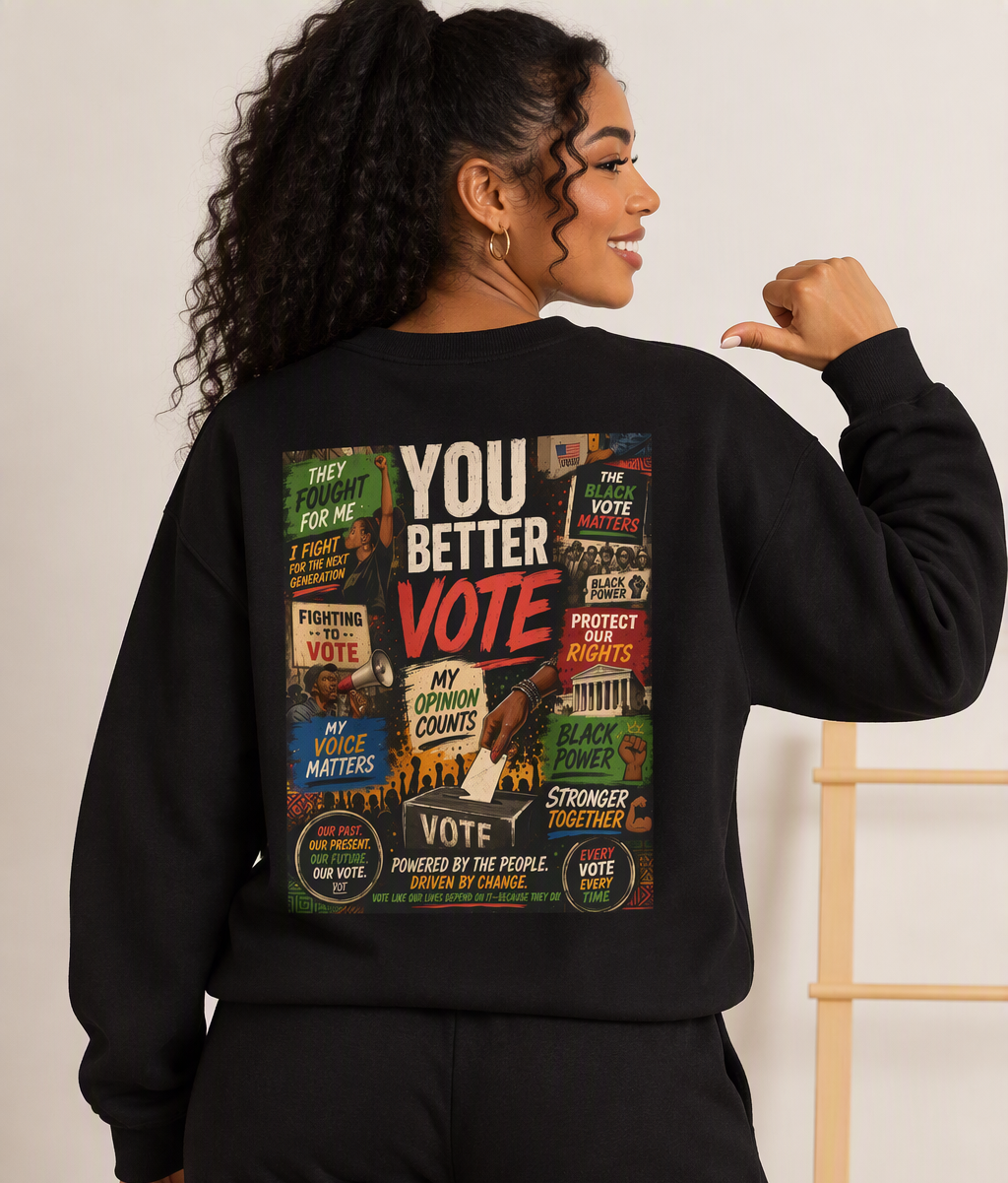 A woman shown from the back wearing a black sweatshirt with a large multicolor graphic print that reads 'YOU BETTER VOTE' and various protest-style signs, paired with black pants in an indoor setting.