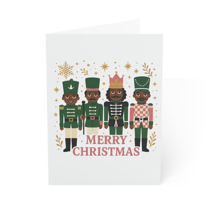 A white Christmas greeting card featuring an illustration of four nutcracker figures in green, pink, and gold, with the text 'MERRY CHRISTMAS' below them, shown on a clean white background.