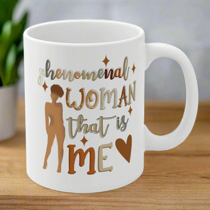 Two white ceramic mugs with the text 'Phenomenal Woman That's Me' printed in brown and gold colors, displayed on a wooden table.