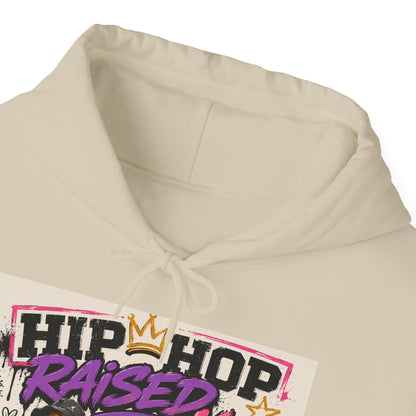 Close-up of a cream-colored hoodie with a graphic print on the front that reads 'HIP HOP RAISED' in black and purple lettering with a gold crown, on a white background.
