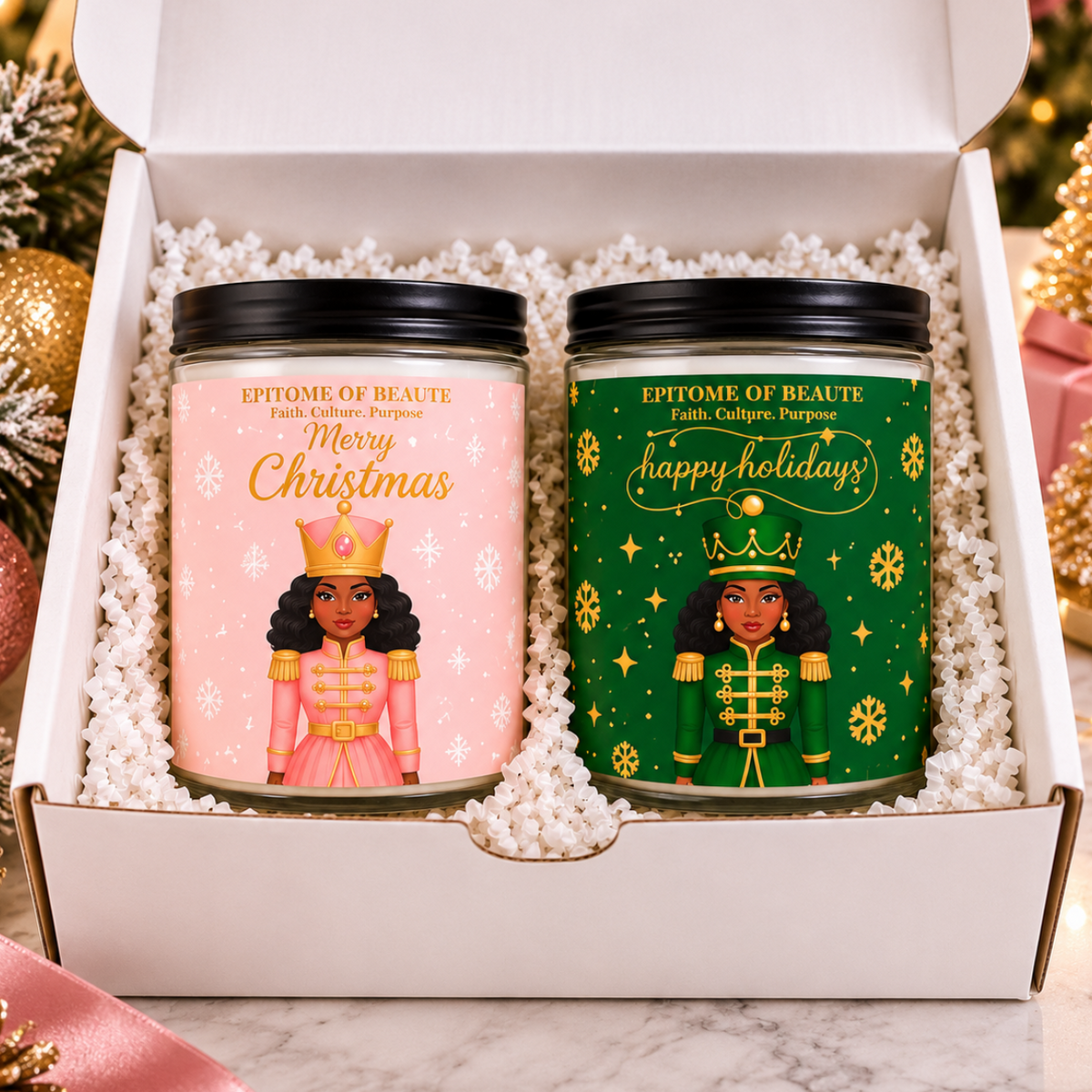 Two personalized Christmas candles in glass jars with black lids, presented in a white gift box filled with white faux fur. The left candle has a pink label with a Nutcracker illustration and reads 'Epitome of Beaute' and 'Merry Christmas'.